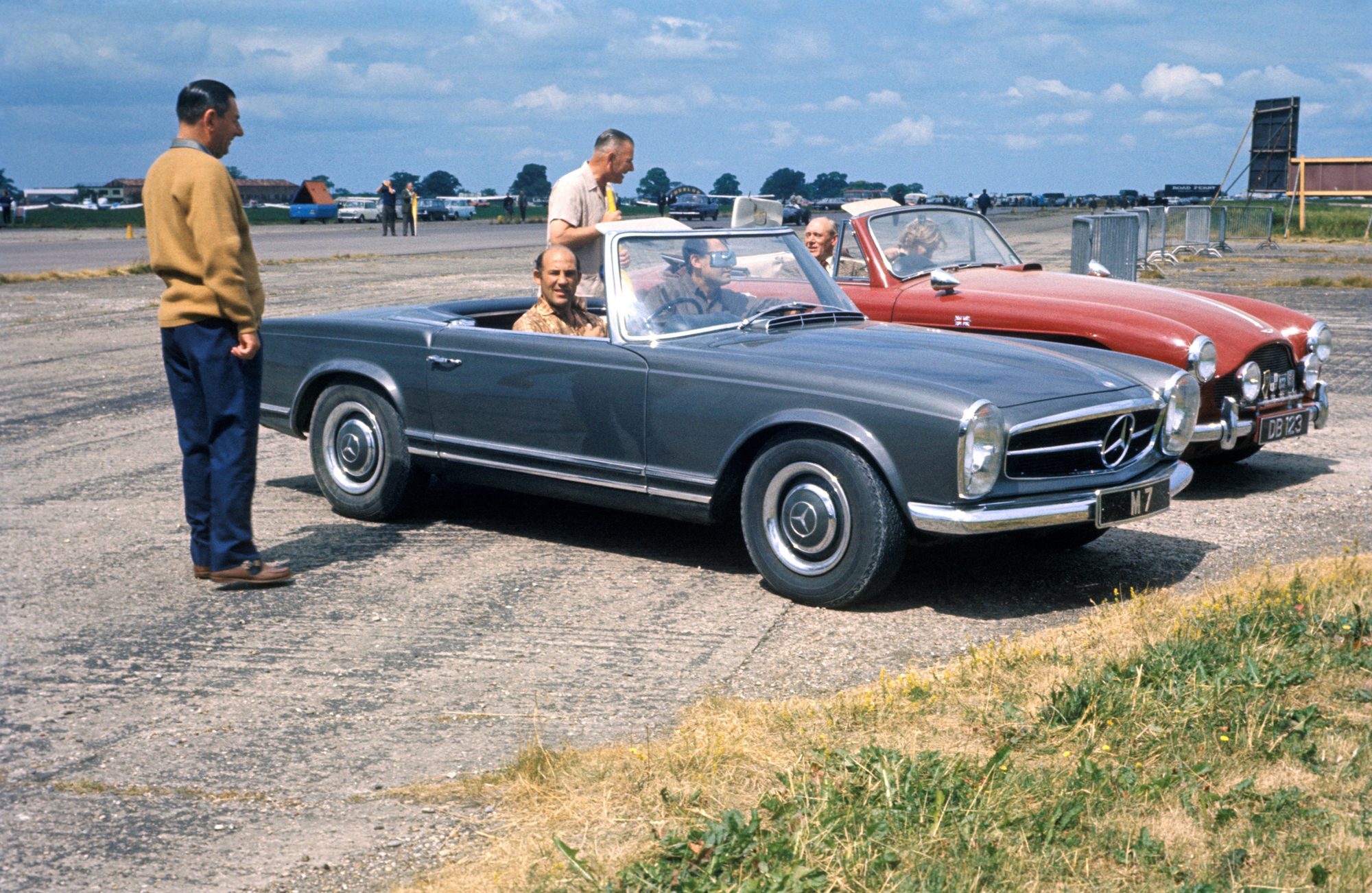 Archive colour photograph of a grey Mercedes-Benz Pagoda parked on an airfield beside a red open-top sports car