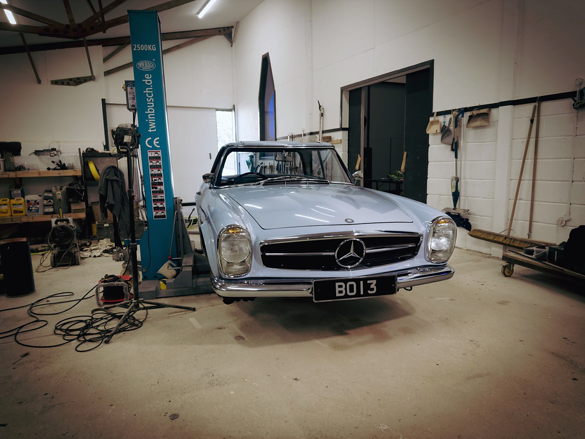 Pale blue Mercedes-Benz Pagoda seen from the front in the workshop, beside a two-post lift